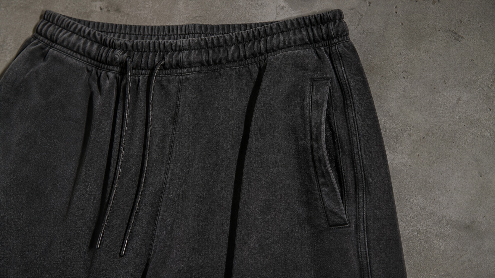 Close digital design detail of the WIDE SWEATPANTS showing the elastic waistband, black drawcord, pocket opening, seam construction and washed-black fabric texture; no internal brand label