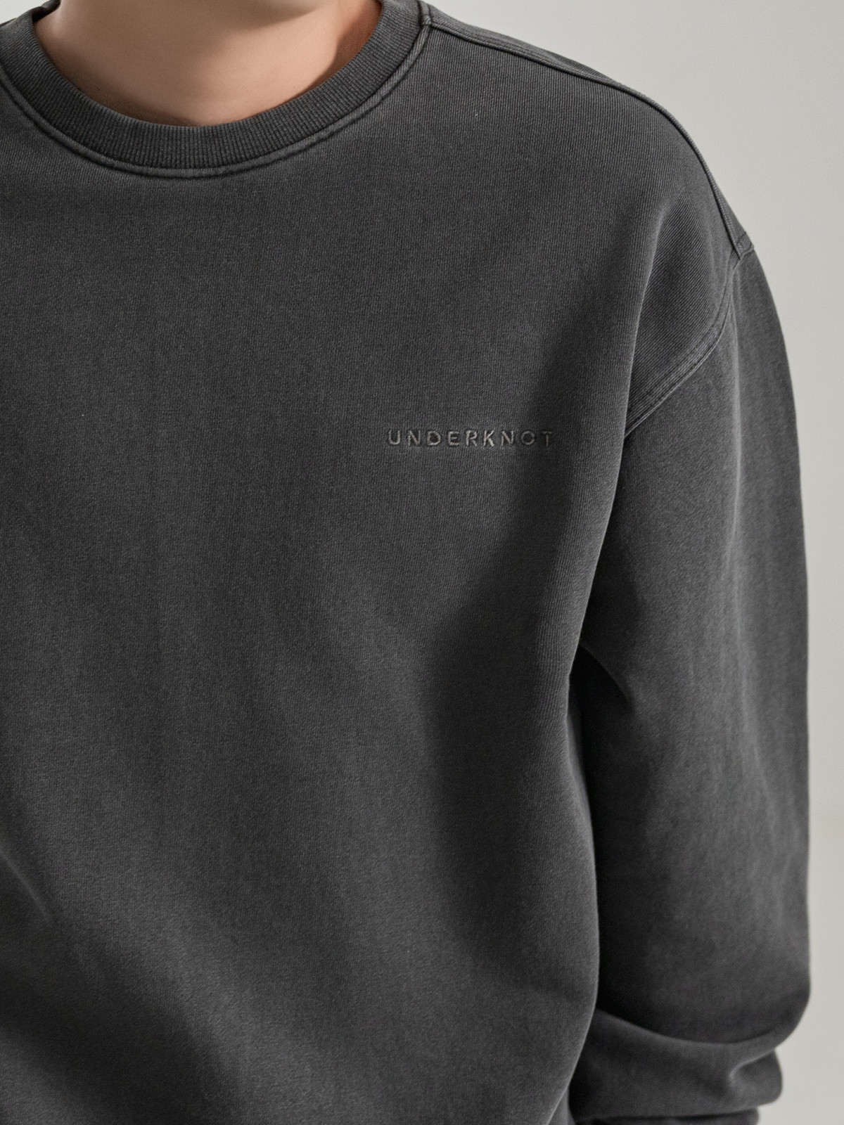 Real studio close-up of the UNDERKNOT chest wordmark embroidery on the WASHED CHARCOAL sweatshirt