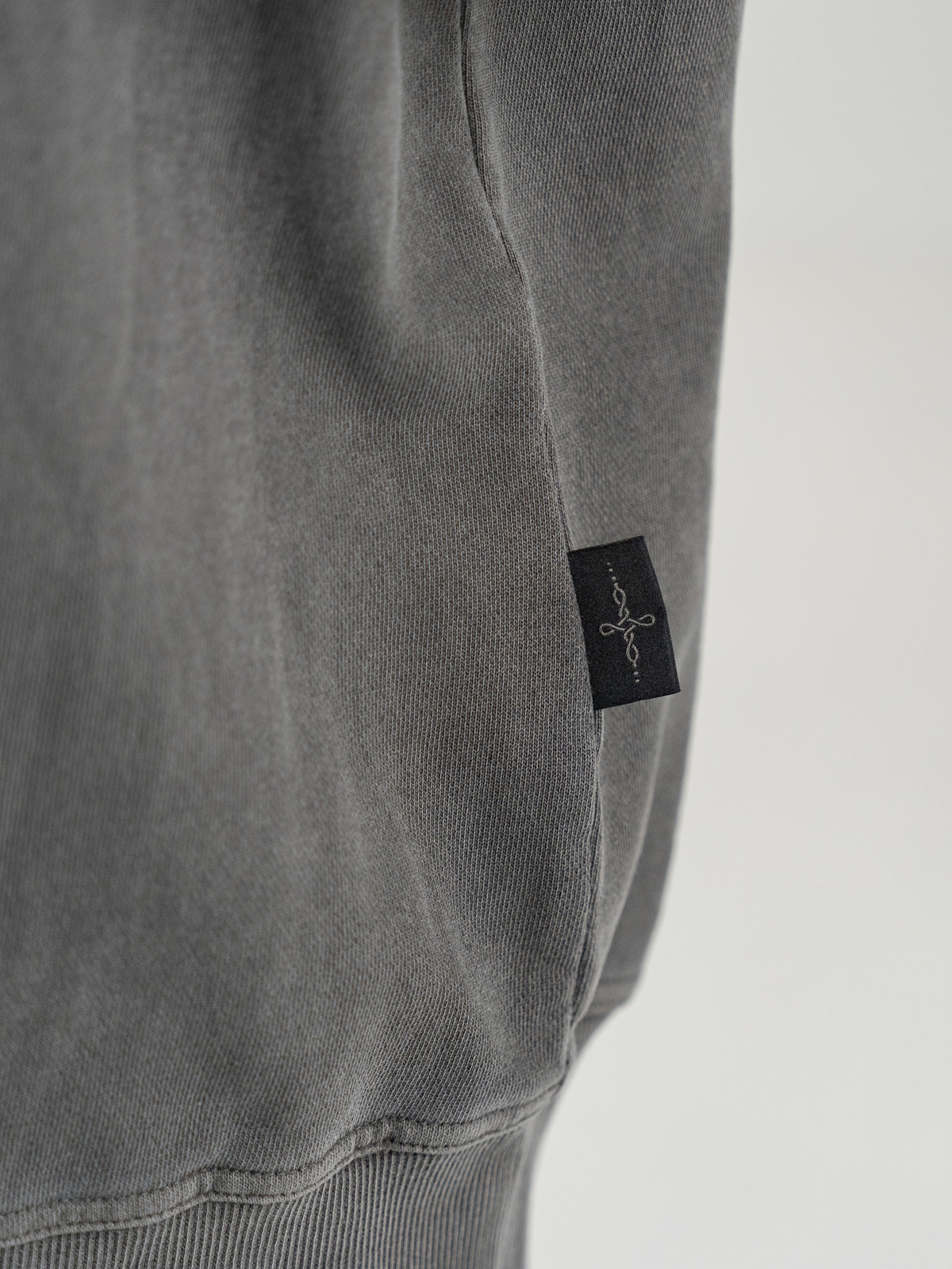 Real studio photograph of UNDERKNOT sweatshirt side-seam stitching, ribbed hem and tag