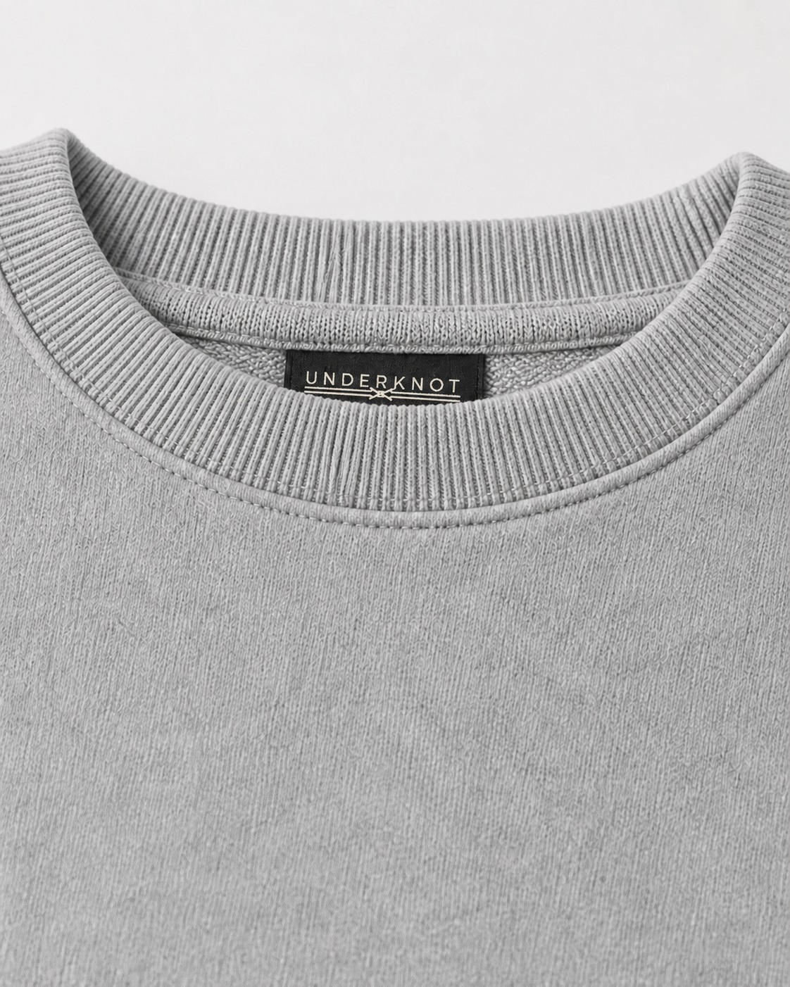BASIC CREWNECK SWEATSHIRT 넥 안쪽 중앙의 블랙 직조 UNDERKNOT 메인라벨과 웜 에크루 엠블럼을 보여 주는 디지털 디테일. 사이즈 표기 없음